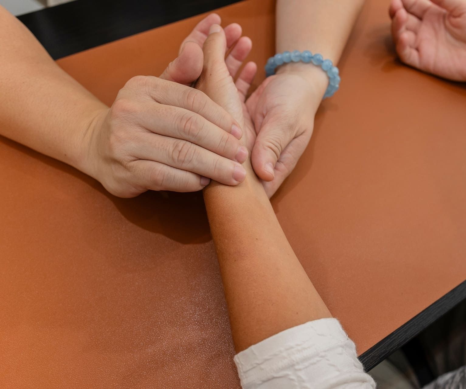 Zwei Hände tasten das Handgelenk einer dritten Person auf braunem Untergrund ab